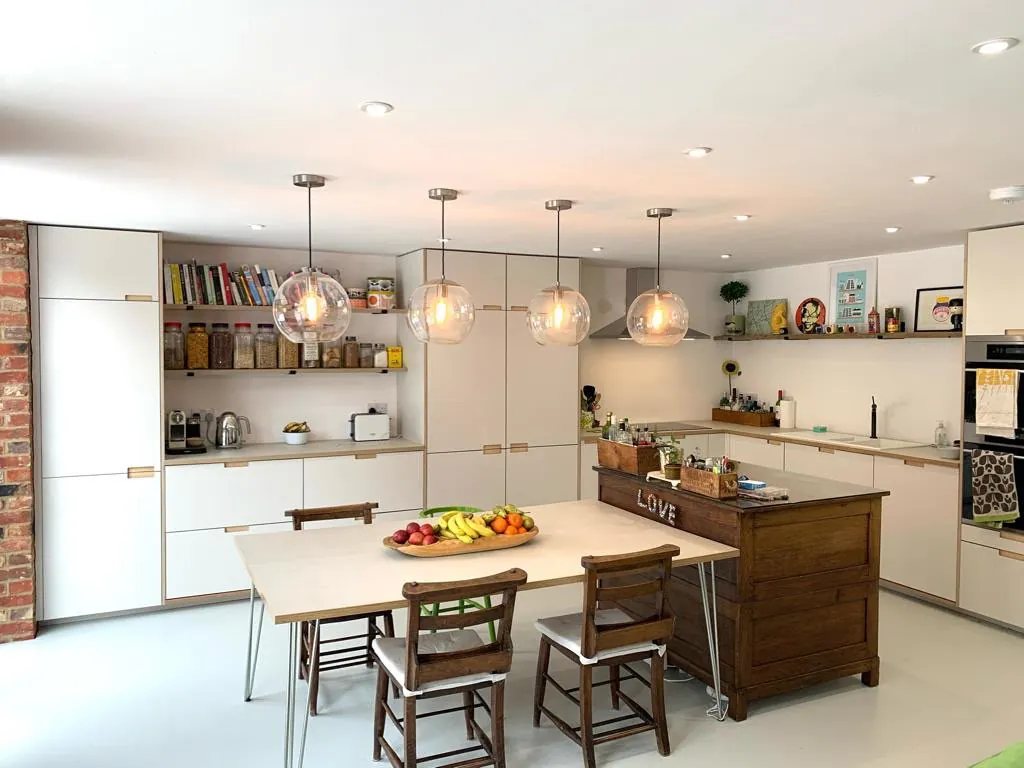 The same room after fitting: cream handleless kitchen with an island, open shelving and the four glass pendants
