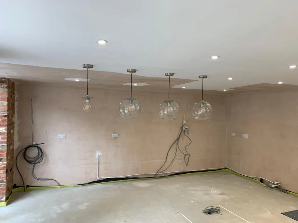 Kitchen before we started: bare plastered walls, capped services and the pendant lights already hung